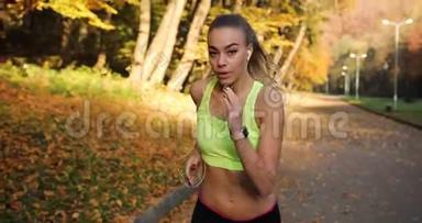 公园里的女跑步者。 女人在镜头前直勾勾地看着，而她却在秋天公园的小径上奔跑